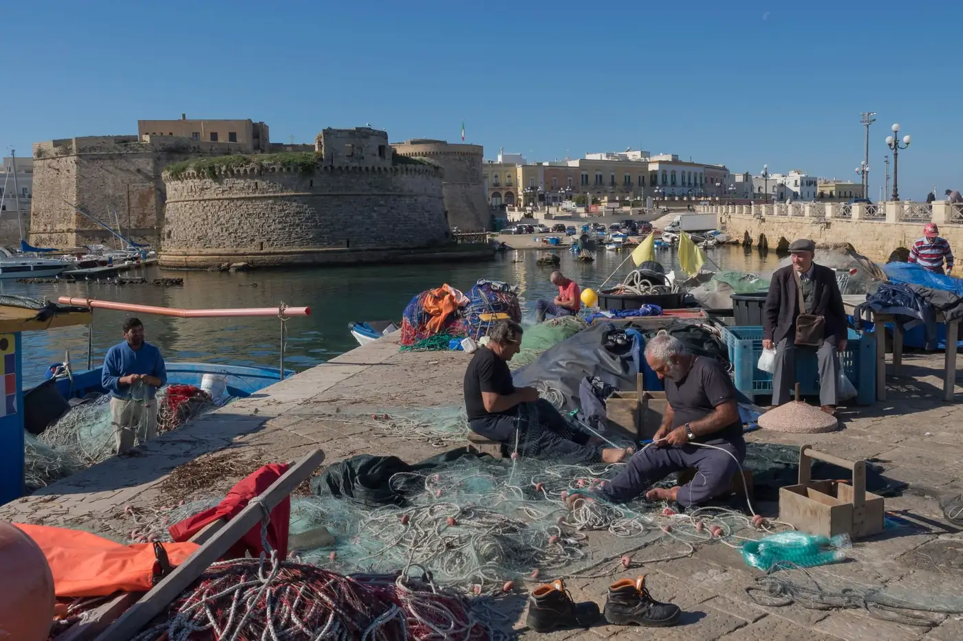 Fishermen mending nets by the medieval castle in Gallipoli, Italy.
