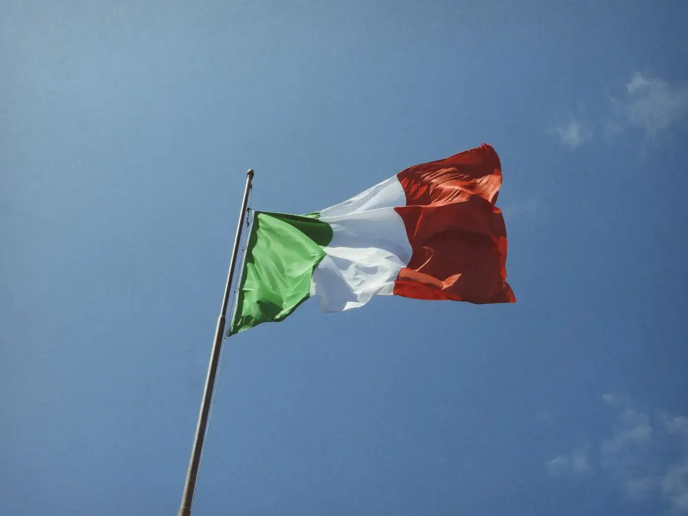 Low angle shot of the Italian flag waving against a clear blue sky.