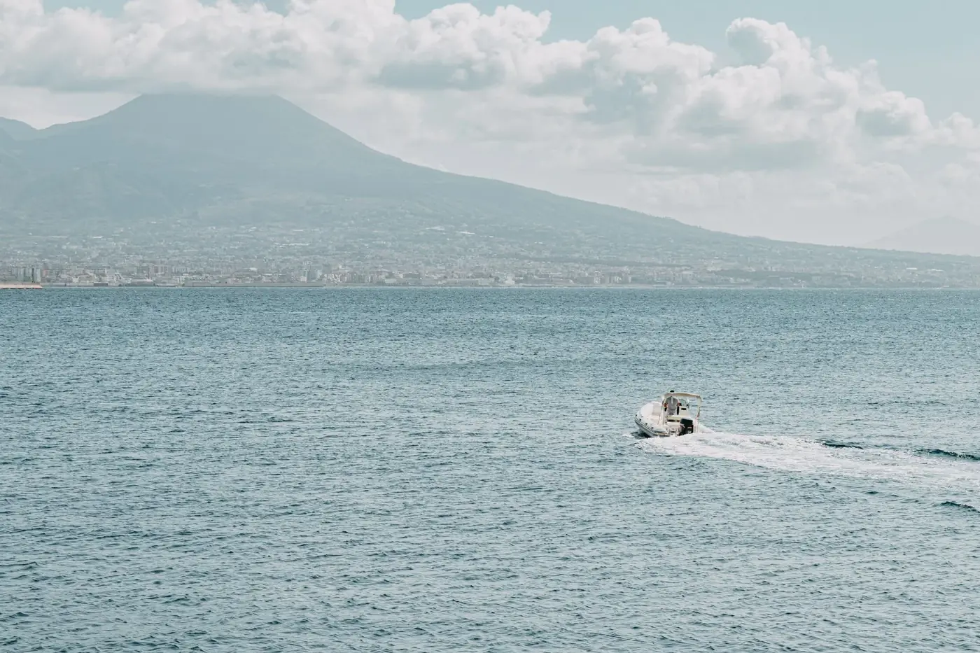 A motorboat glides on the sea with Mount Vesuvius in the background, near Naples, Italy.