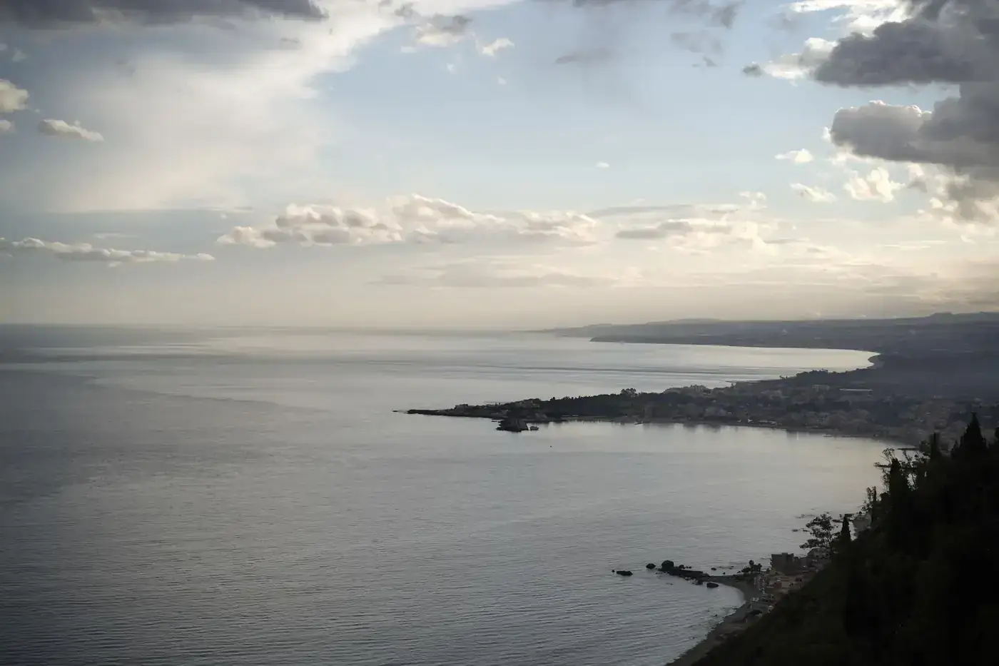 Picturesque seascape of Taormina, Sicily, featuring tranquil waters and dramatic clouds at dusk.