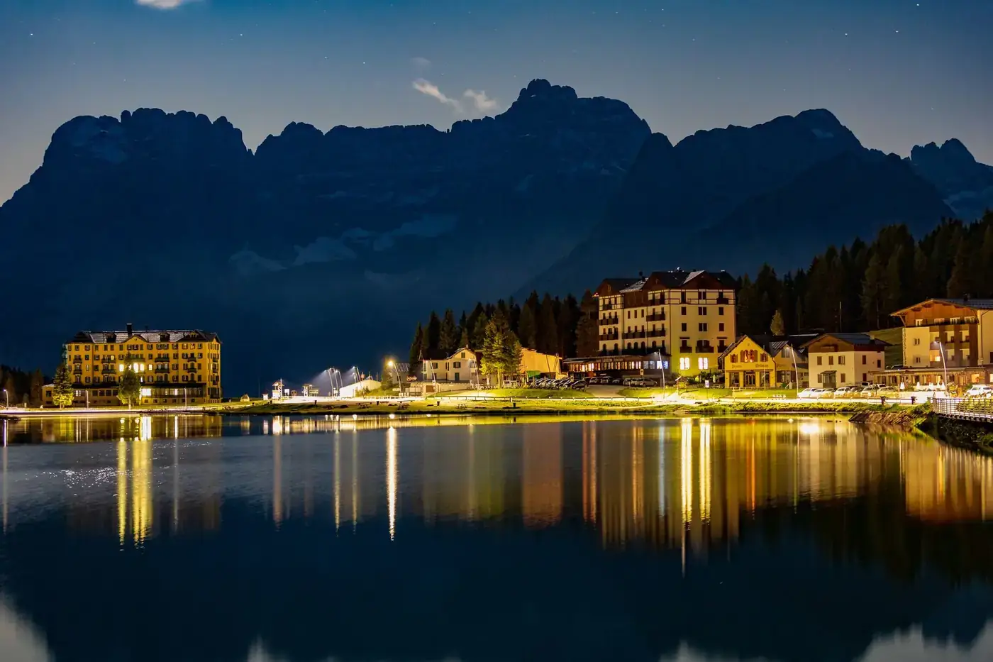 Scenery of peaceful pond surrounded by dwelling houses on shore against mountains in highland at night