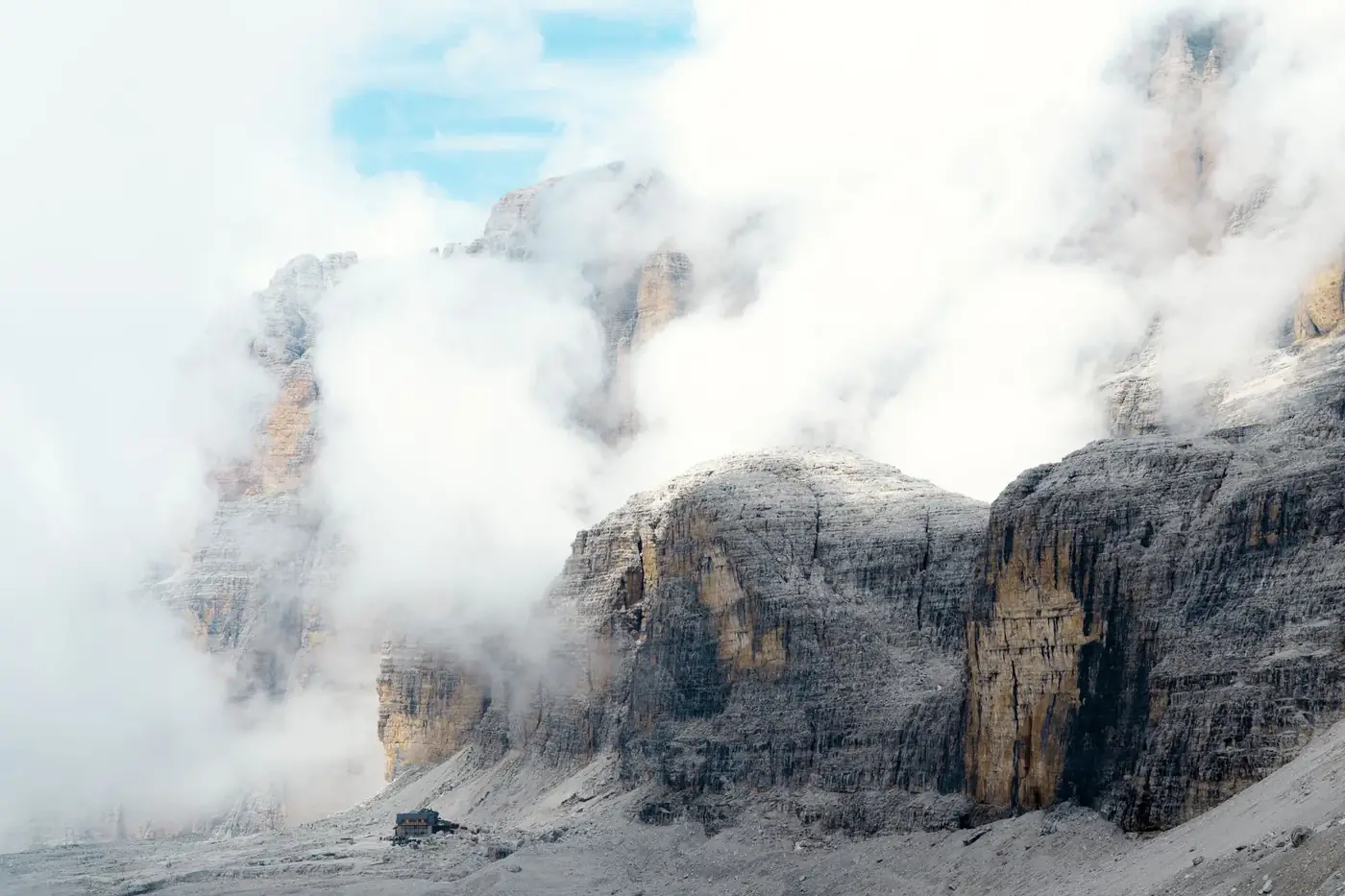 A serene view of misty mountains in the Dolomites with a solitary stone hut nestled amid fog and clouds.