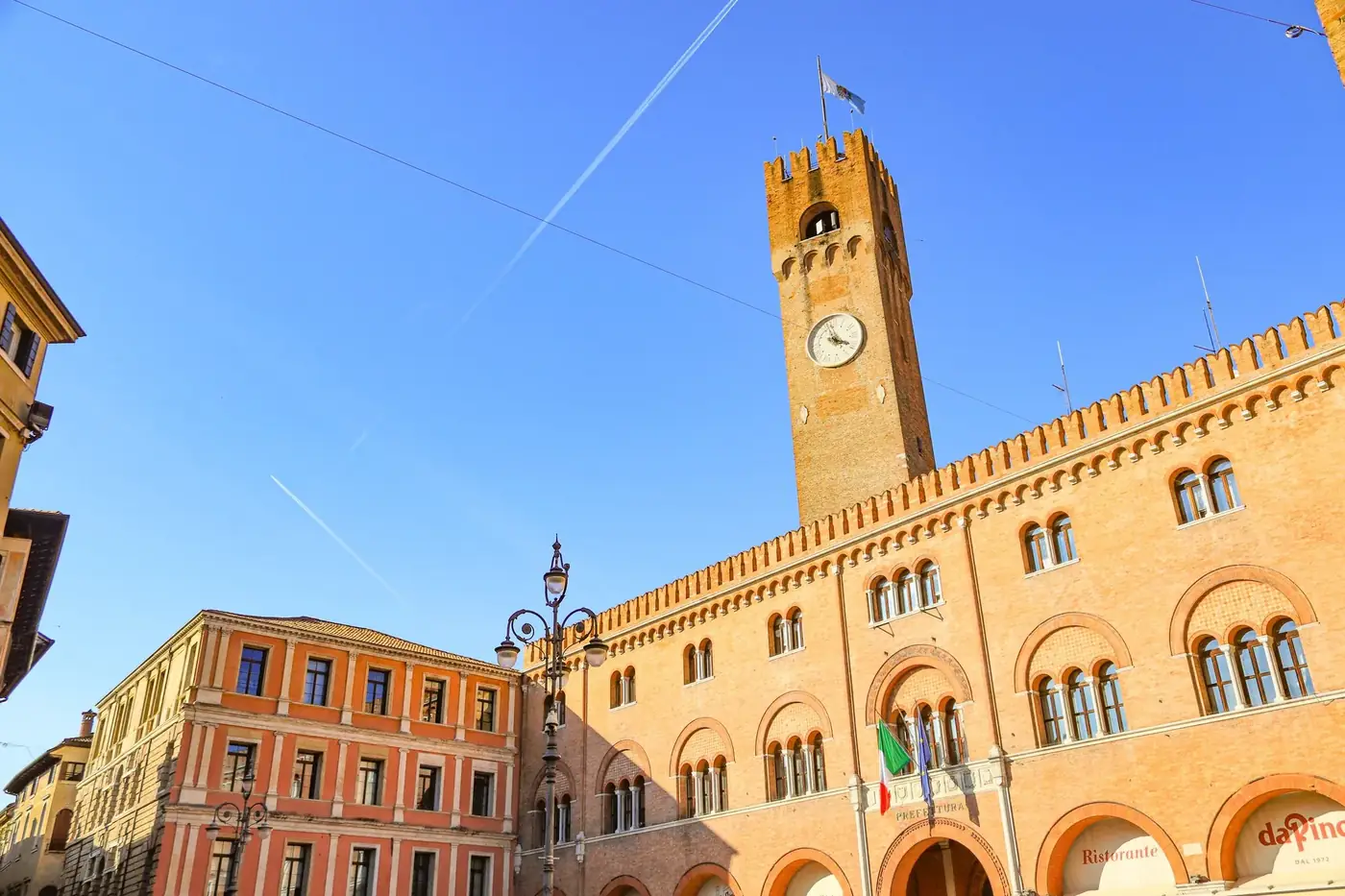Sunlit view of Treviso's clock tower and historic buildings against a blue sky.
