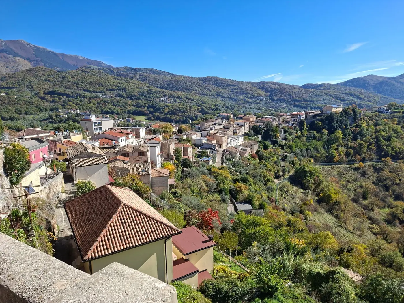 Charming hillside village with lush greenery and terracotta roofs in a mountainous landscape.