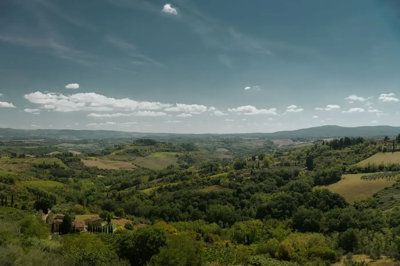 A breathtaking view of the lush green hills and fields of San Gimignano, Tuscany under a clear summer sky.