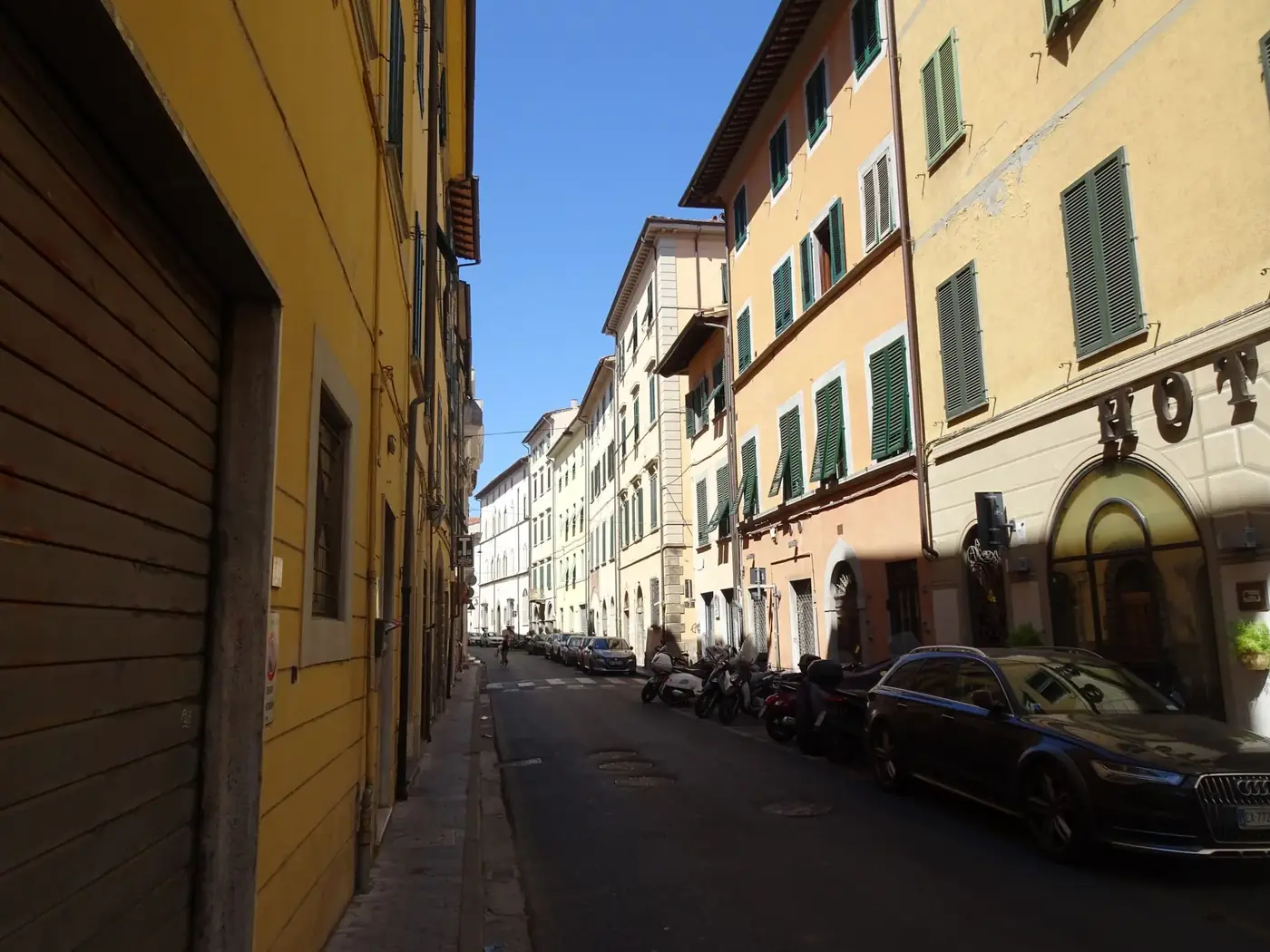 Quaint street scene in Pisa, Tuscany, Italy showcasing colorful buildings and parked vehicles.
