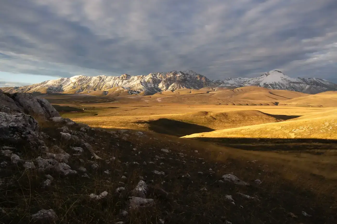 Breathtaking view of snow-capped mountains and rolling hills under dramatic skies in Abruzzo, Italy.