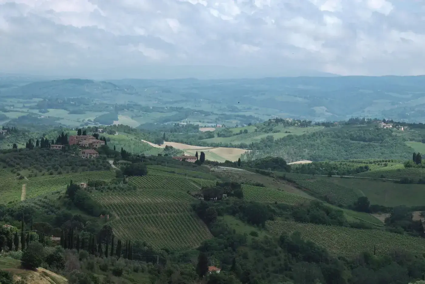 Stunning aerial shot of Tuscany's rural landscape with vineyards and rolling hills under a cloudy sky.
