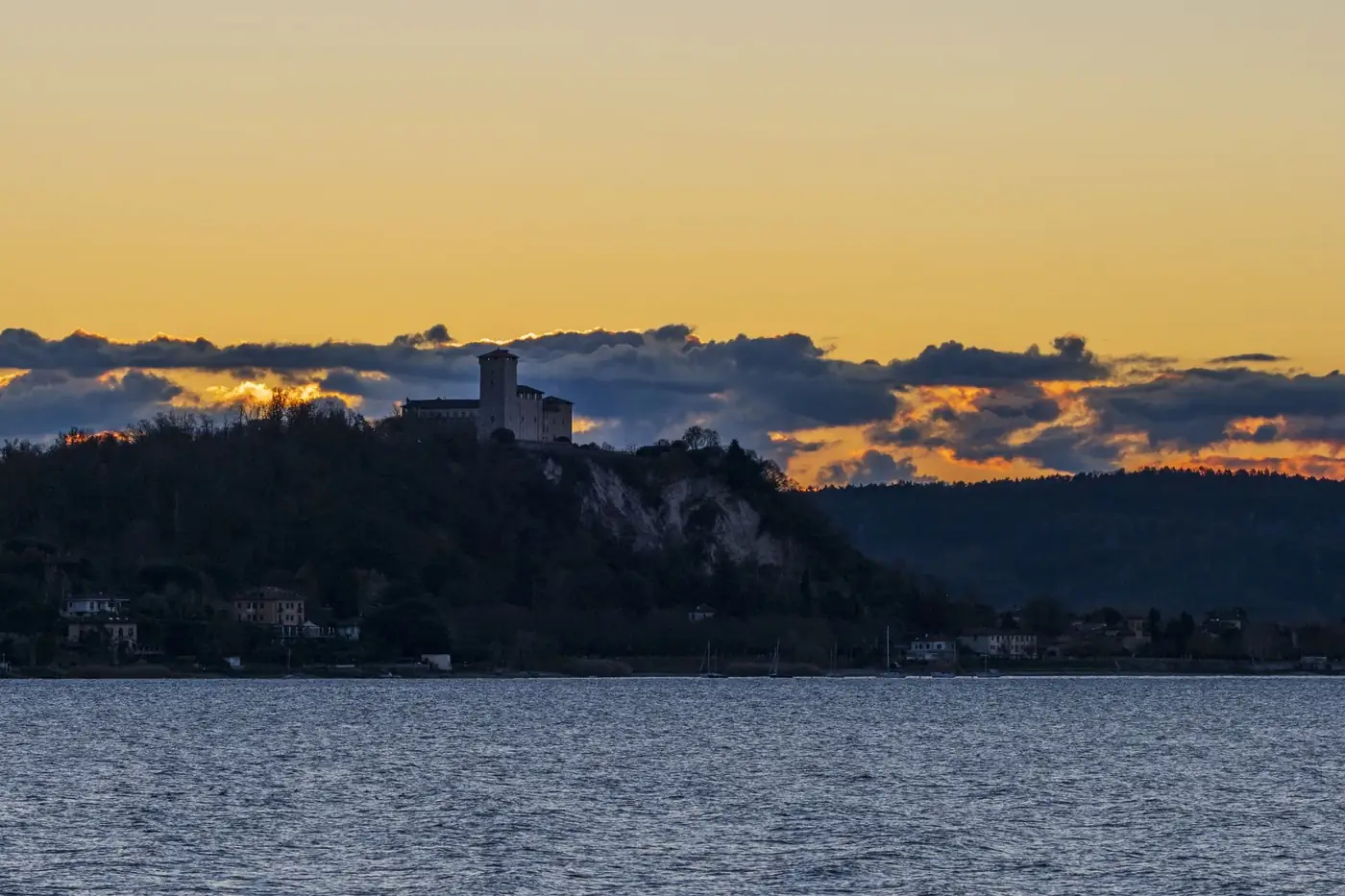 Silhouette of a castle on a hill during a vibrant sunset over a lake.