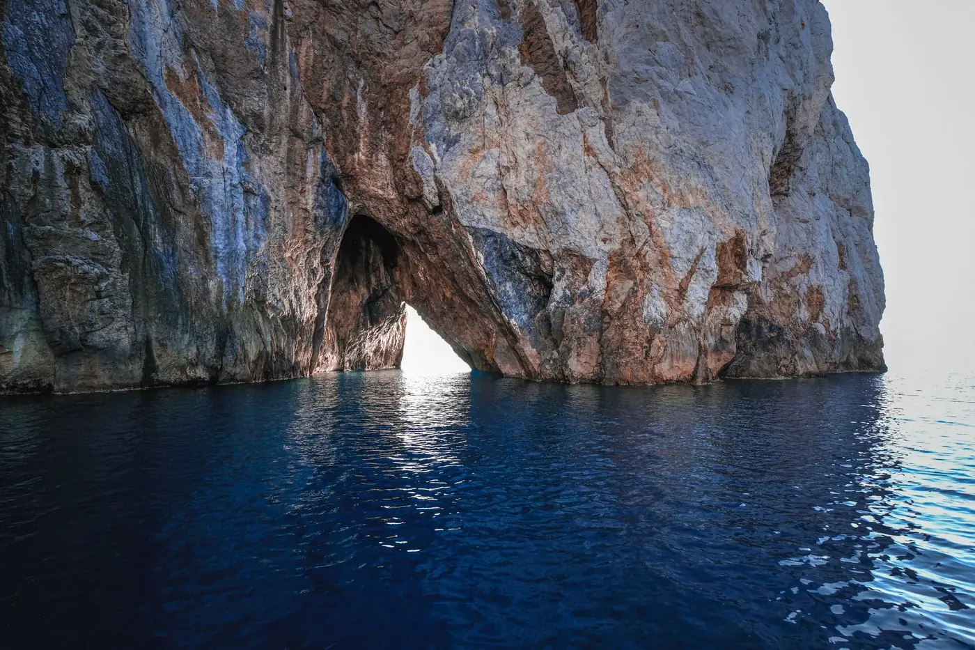 Tall majestic cliffs with rough uneven surface over short water pathway next to vibrant blue bay in daytime