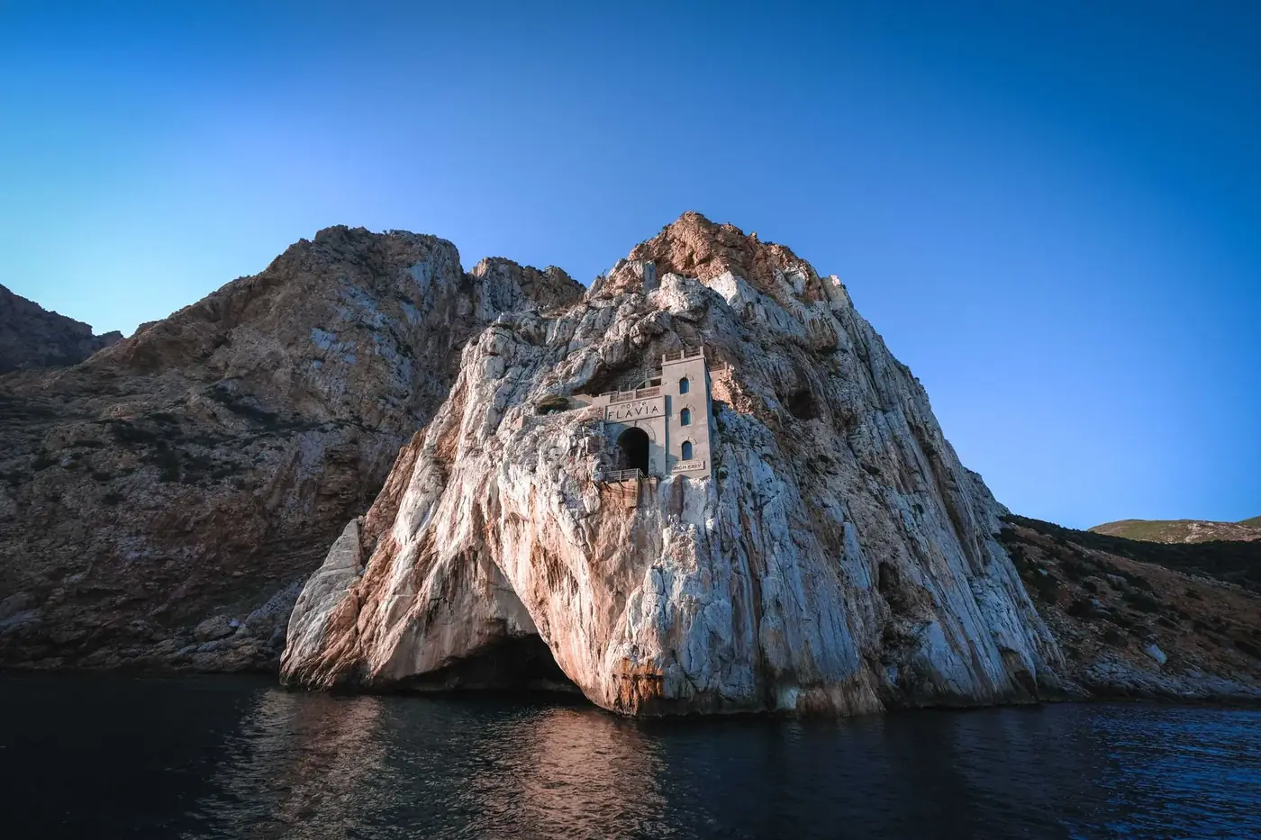 From below amazing landscape of crag with ancient building on it on coastline of calm sea