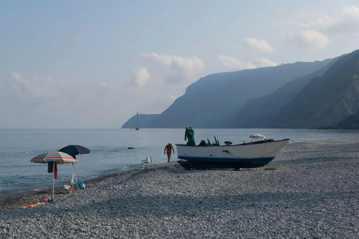 A peaceful beach with a docked boat and hills in the background, Reggio Calabria, Italy.