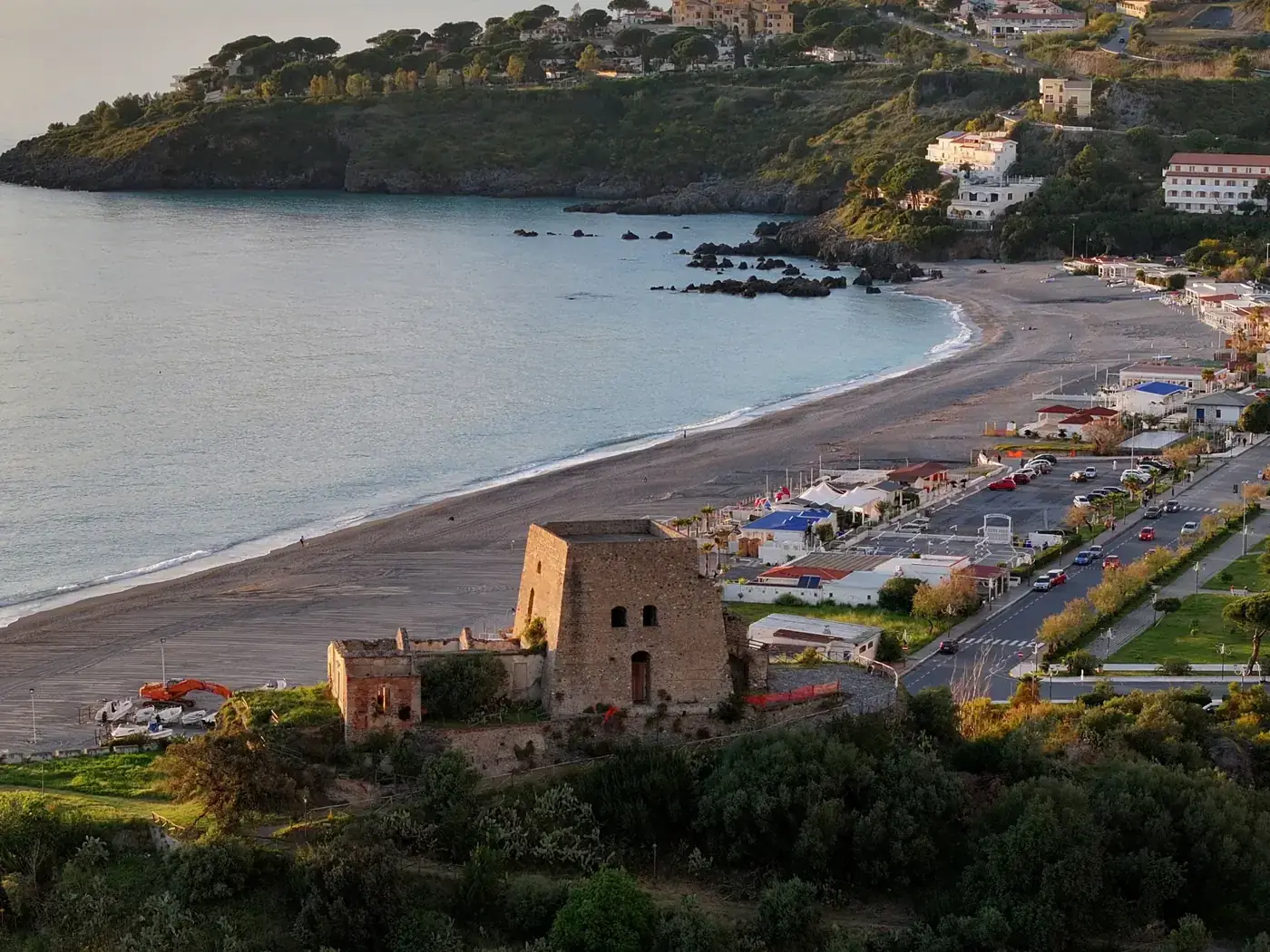 Aerial view of a coastal beach and historic ruins at sunset, featuring stunning natural beauty.