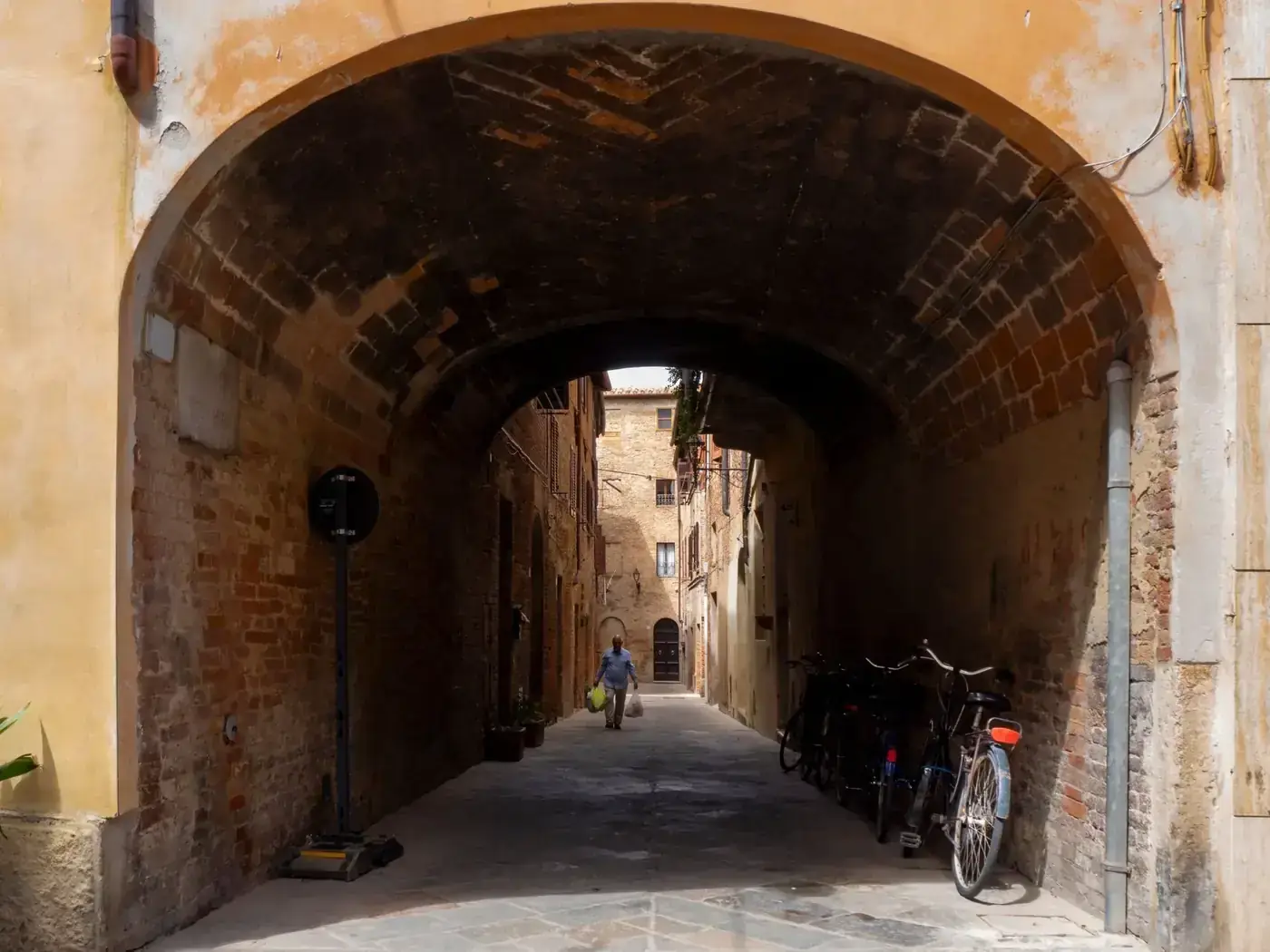 Rustic alleyway under an ancient arch with a cyclist in Buonconvento, Tuscany.