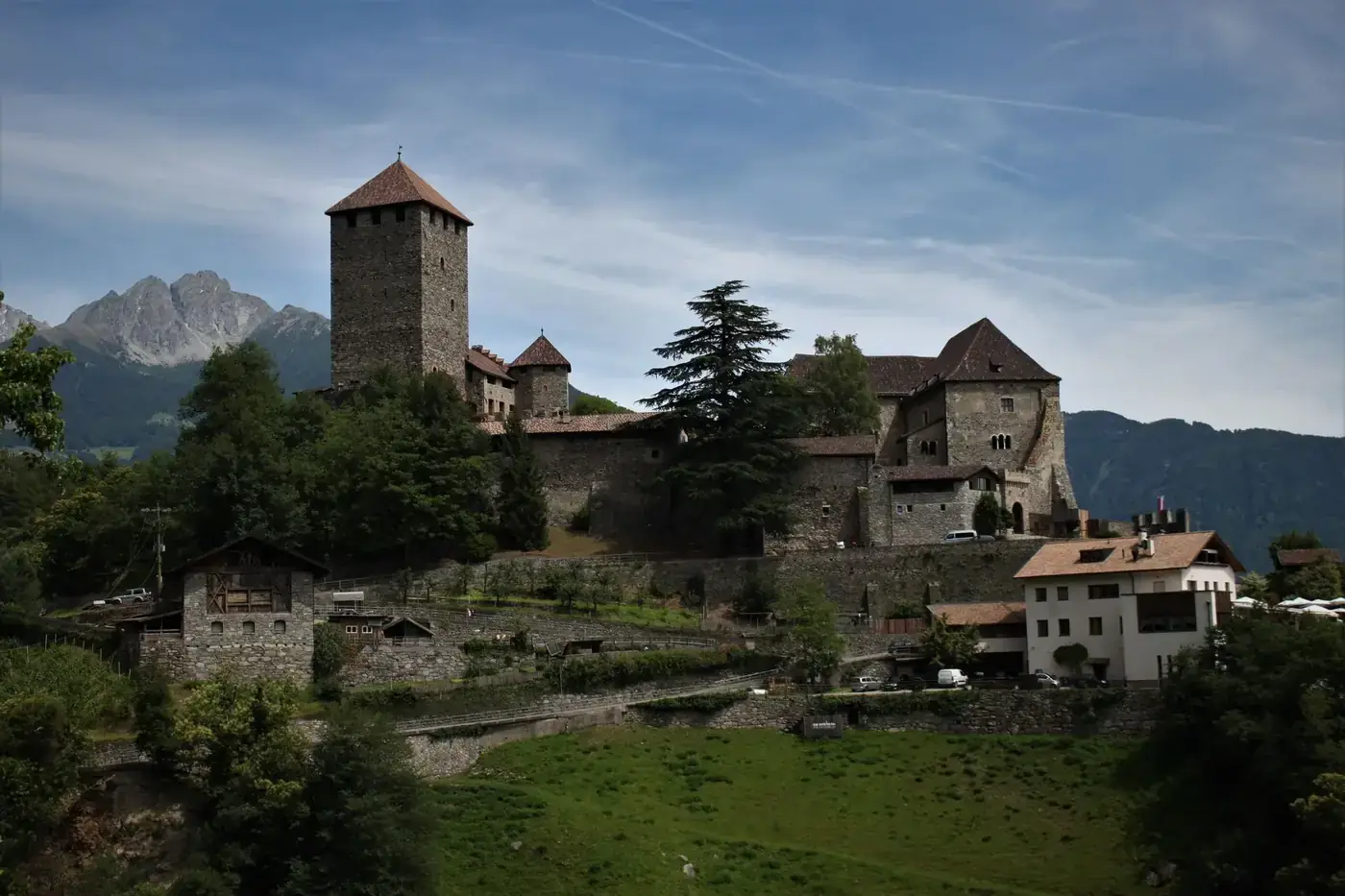 Scenic view of a historic castle in Tirolo, Italy with mountains behind.