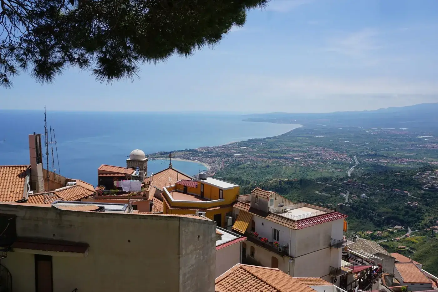 A breathtaking view over Sicilian rooftops and coastline under a bright summer sky.