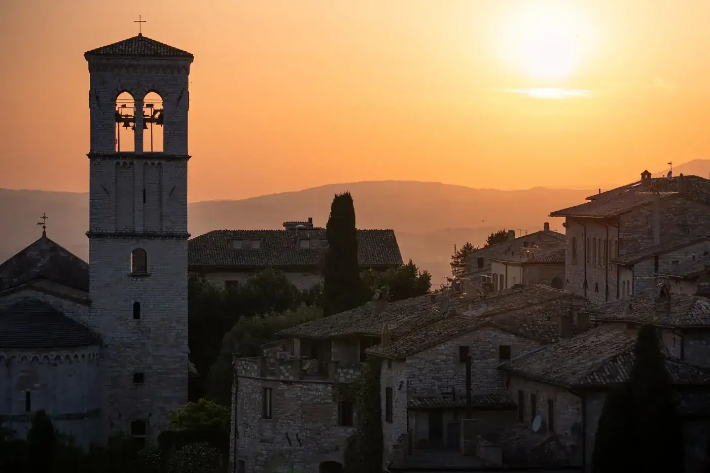 Stunning sunset over the historic stone buildings of Assisi, Italy with a bell tower in view.
