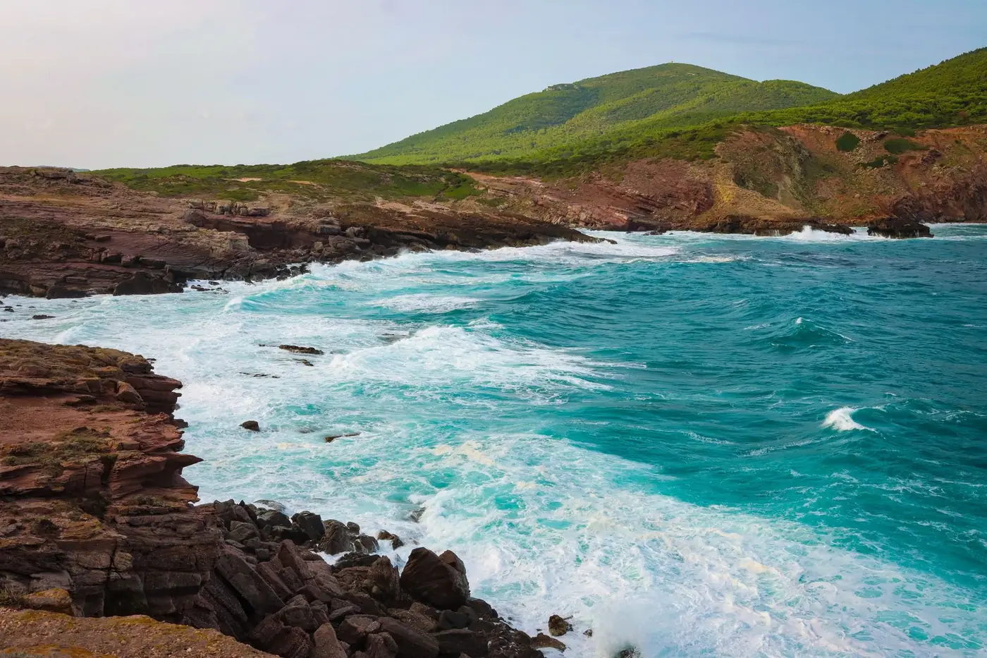 Stunning view of Alghero coastline with rocky cliffs and turquoise waves crashing.