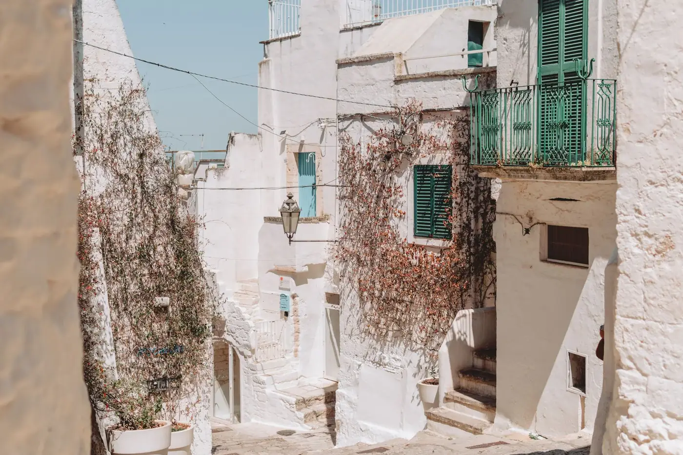 Explore the picturesque alleys of Ostuni, Apulia, with sunlit whitewashed buildings and green shutters.