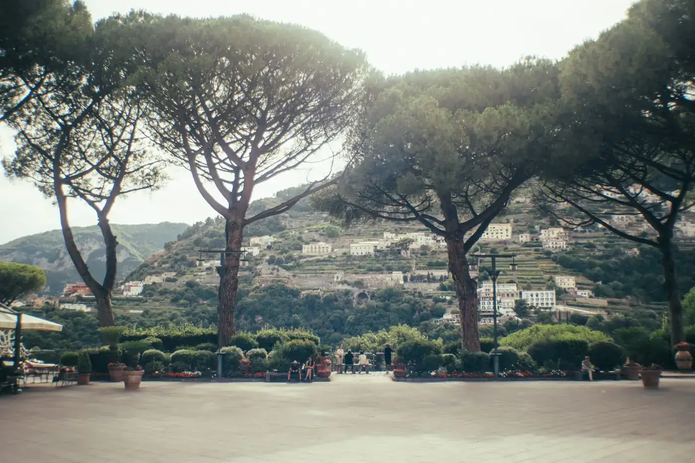 Charming Italian hillside view from a beautiful terrace with lush greenery and distant buildings.
