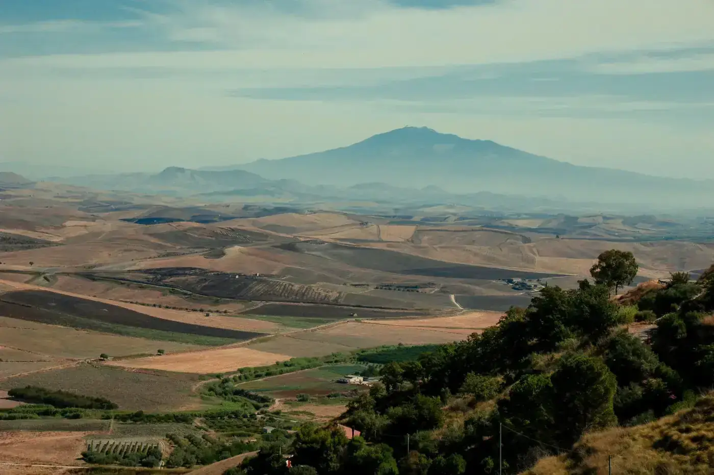 Aerial landscape with rolling hills and Mount Etna in the distance, captured in Catania, Sicily.