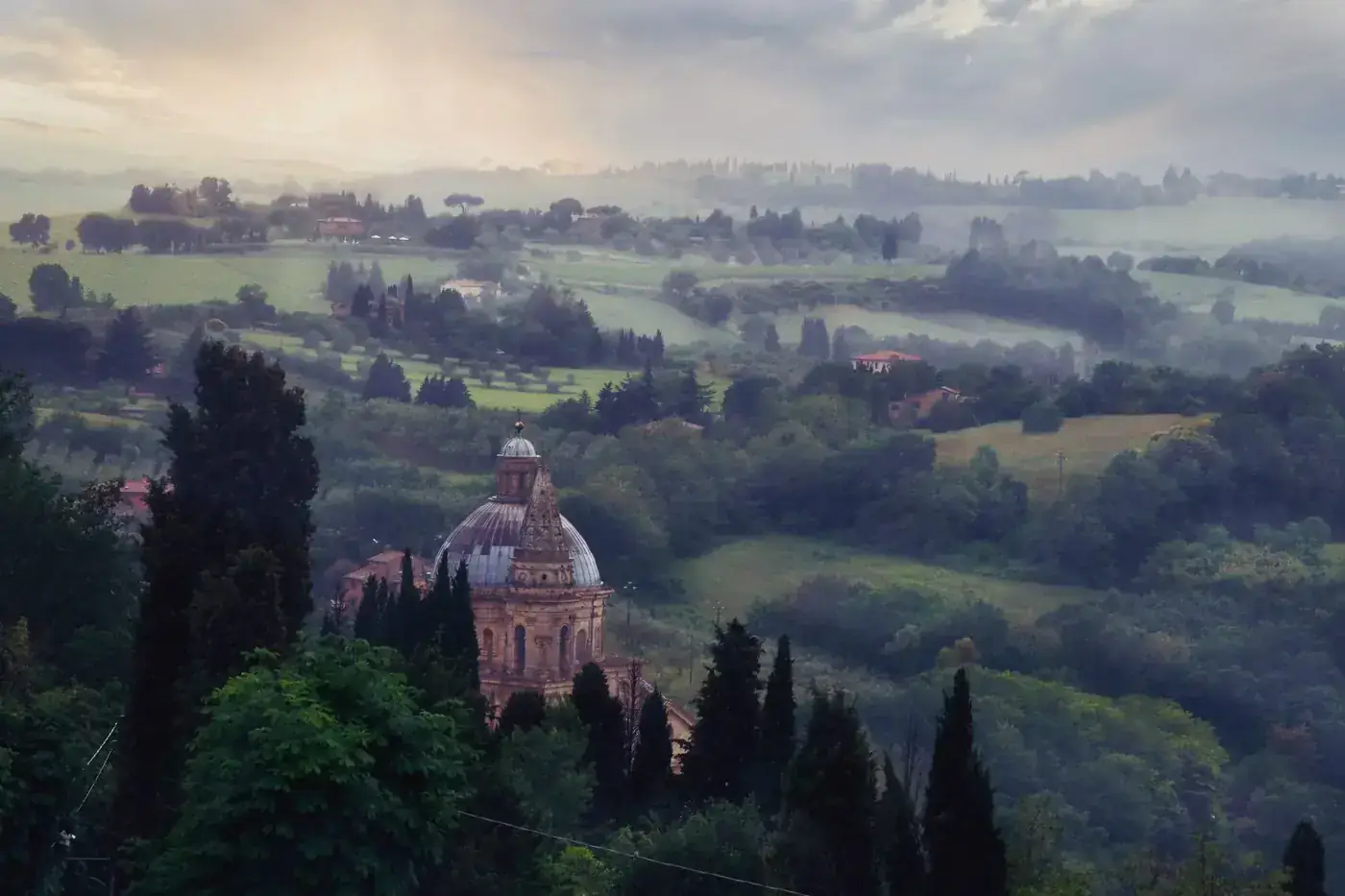 A serene misty landscape in Italy with greenery and historical architecture.
