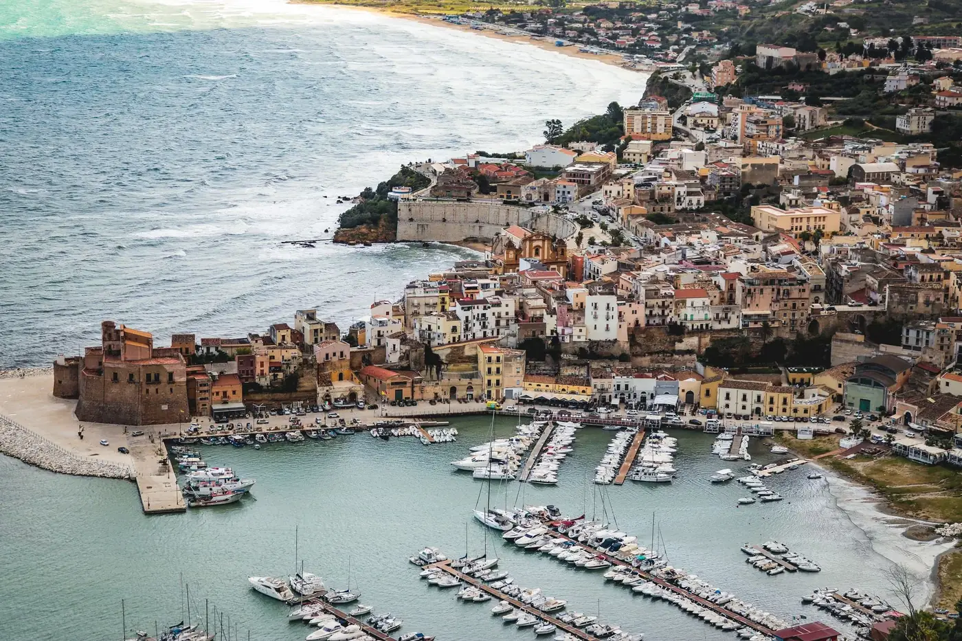 A picturesque aerial shot of a coastal town in Sicily, showcasing the marina and historic architecture.
