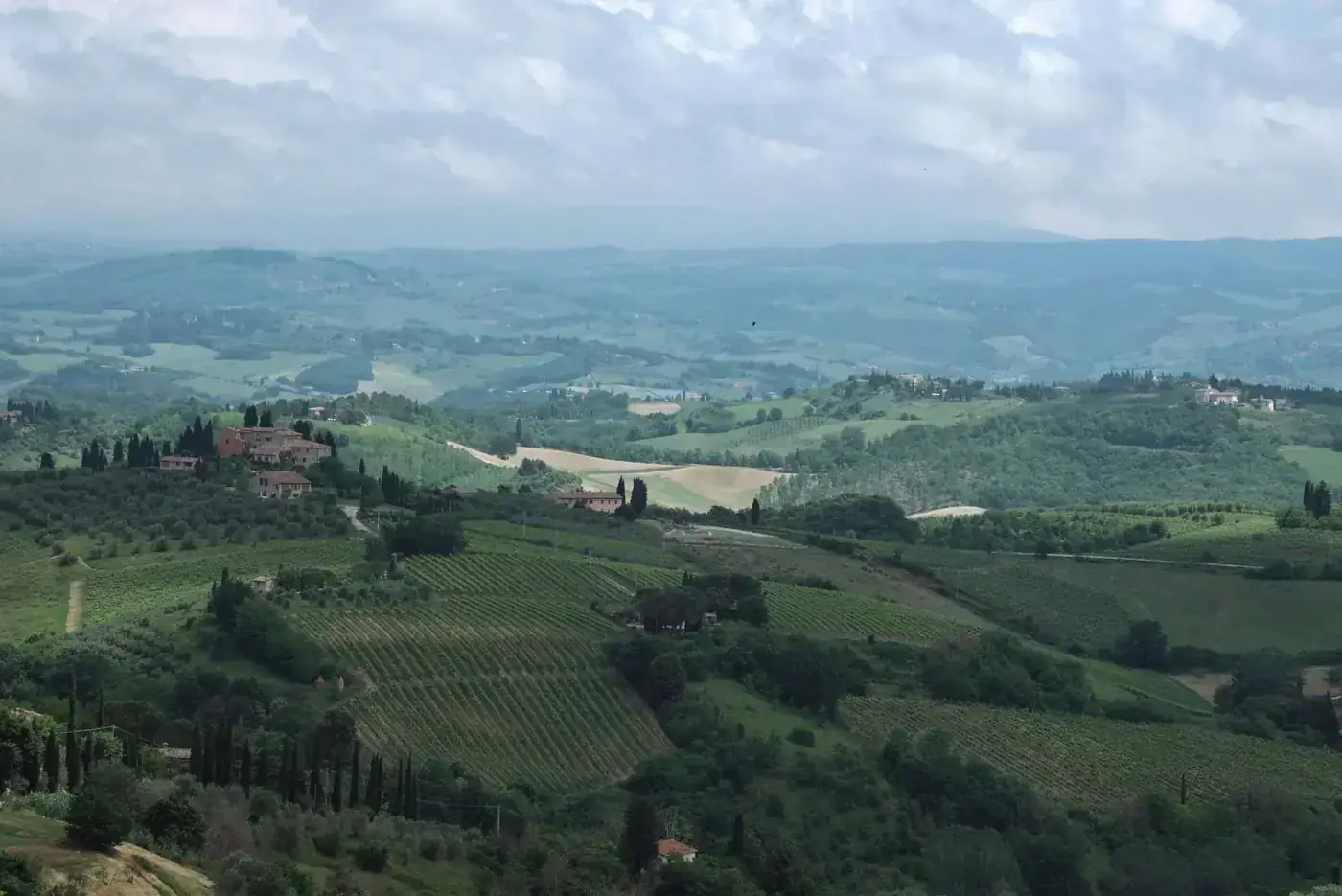 Stunning aerial shot of Tuscany's rural landscape with vineyards and rolling hills under a cloudy sky.