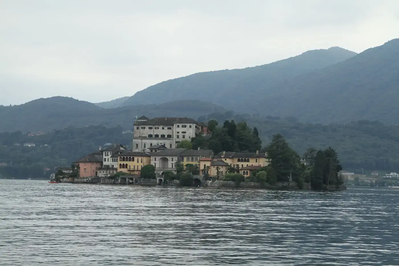Serene view of an island with historical architecture on a tranquil lake surrounded by mountains.