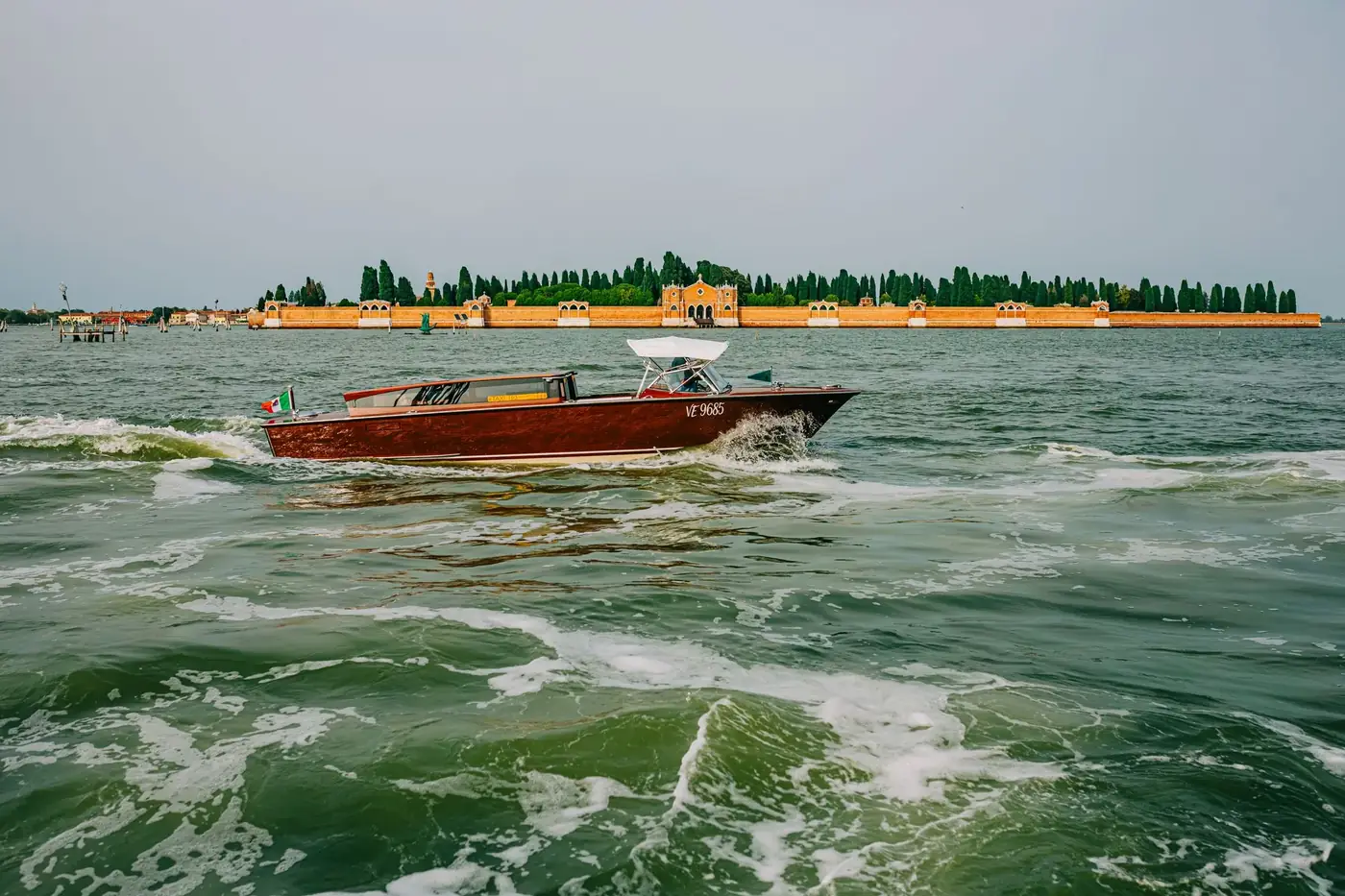 A classic wooden boat navigating the waters near the distinctive cemetery island in Venice, Italy.