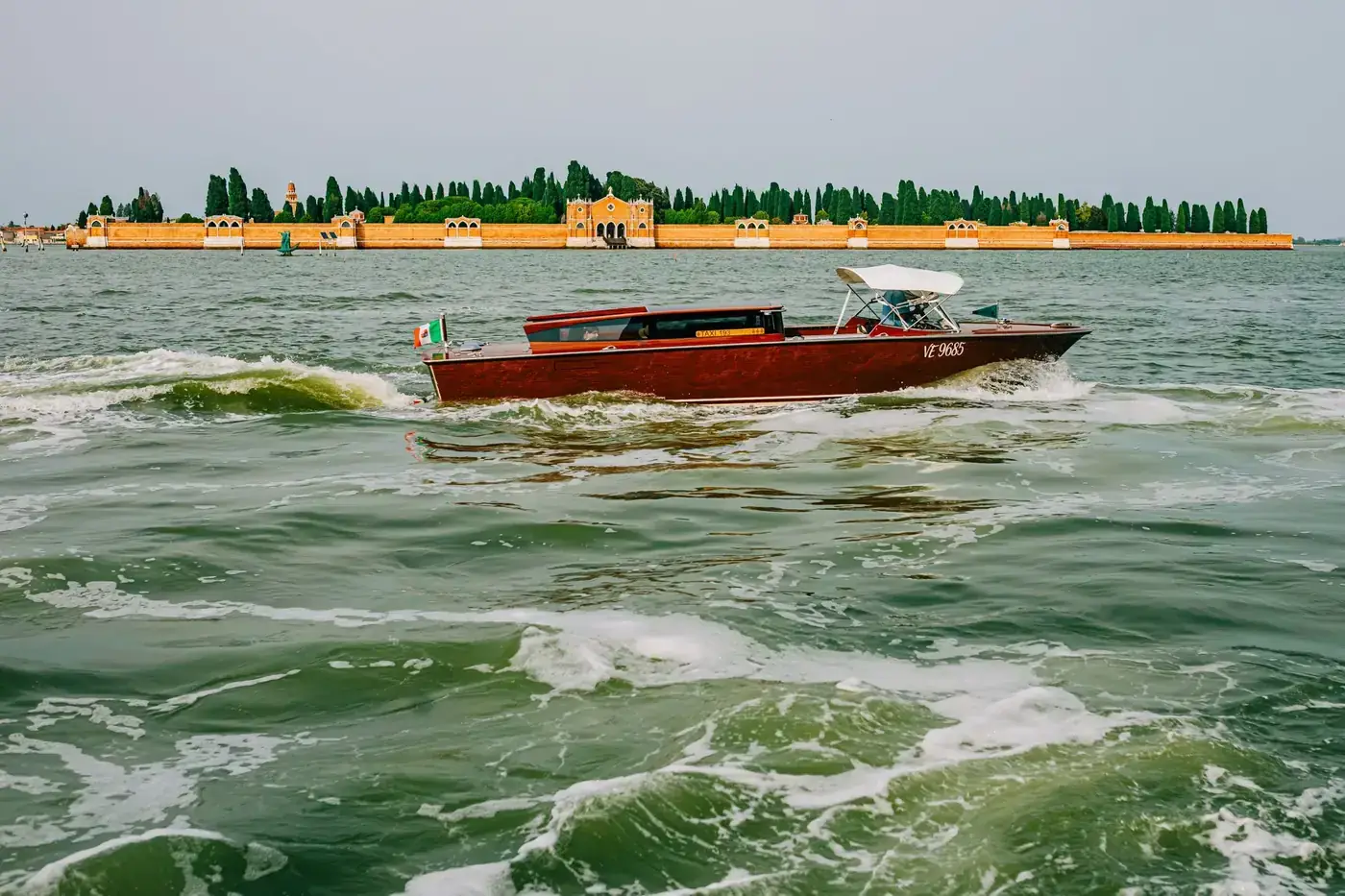 A wooden boat sails near the iconic San Michele Cemetery in Venice.