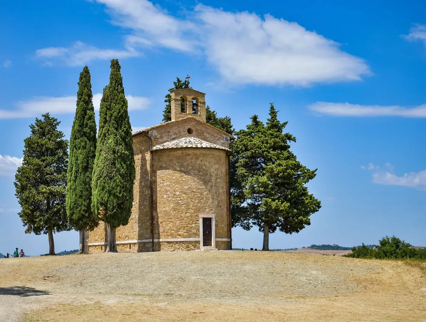 The picturesque Chapel of Vitaleta nestled in the serene Tuscan countryside with lush trees.