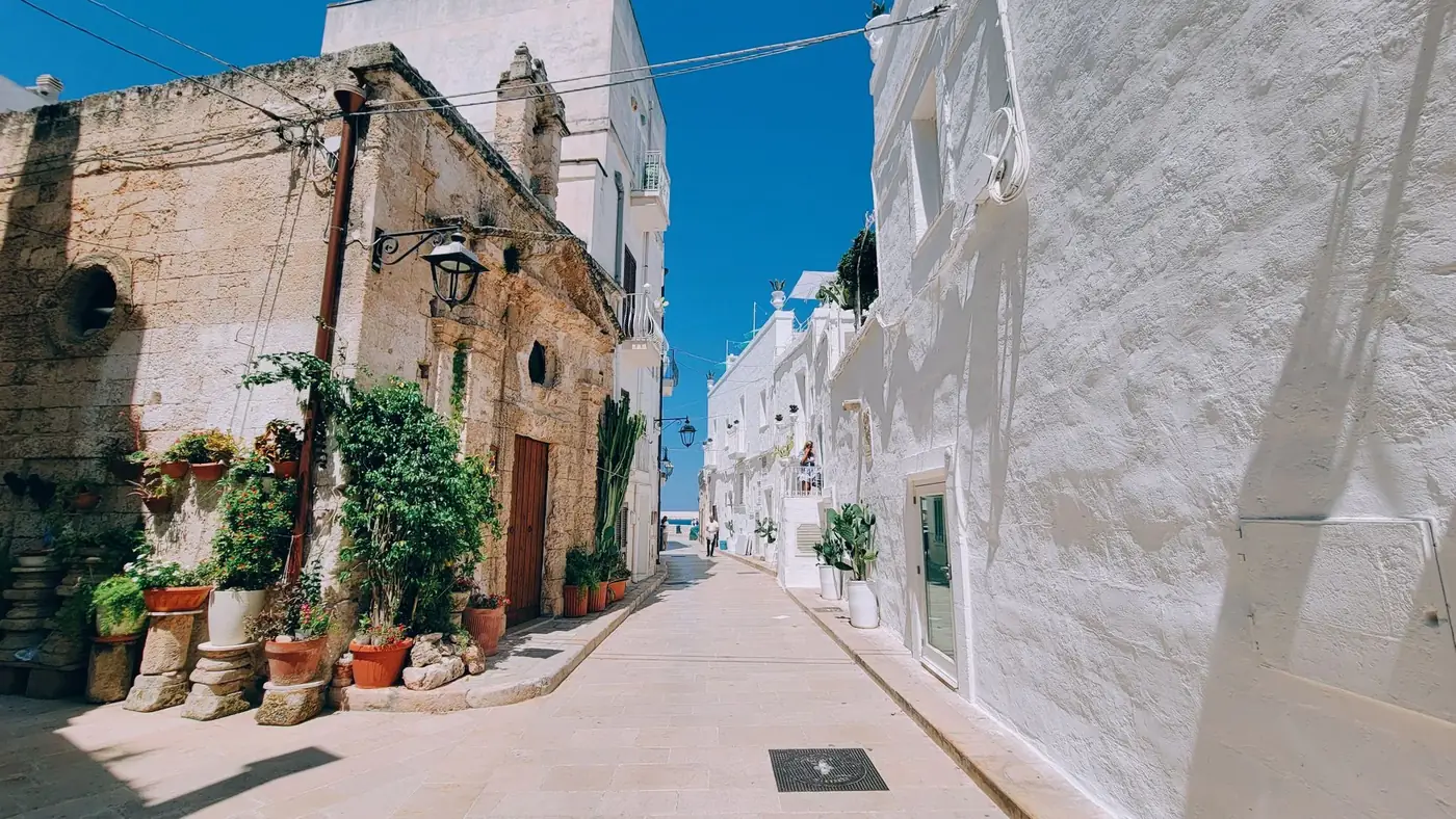 Discover the charming whitewashed alleys of Ostuni, Italy, featuring vibrant plants and stunning architecture under a cl