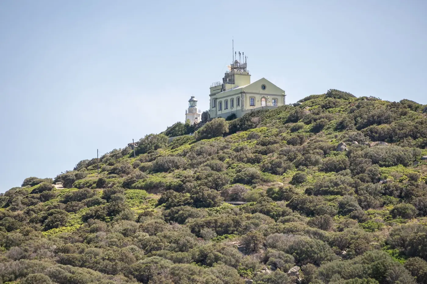 Scenic view of Capo Carbonara Lighthouse atop a lush hill in Villasimius, Sardinia.