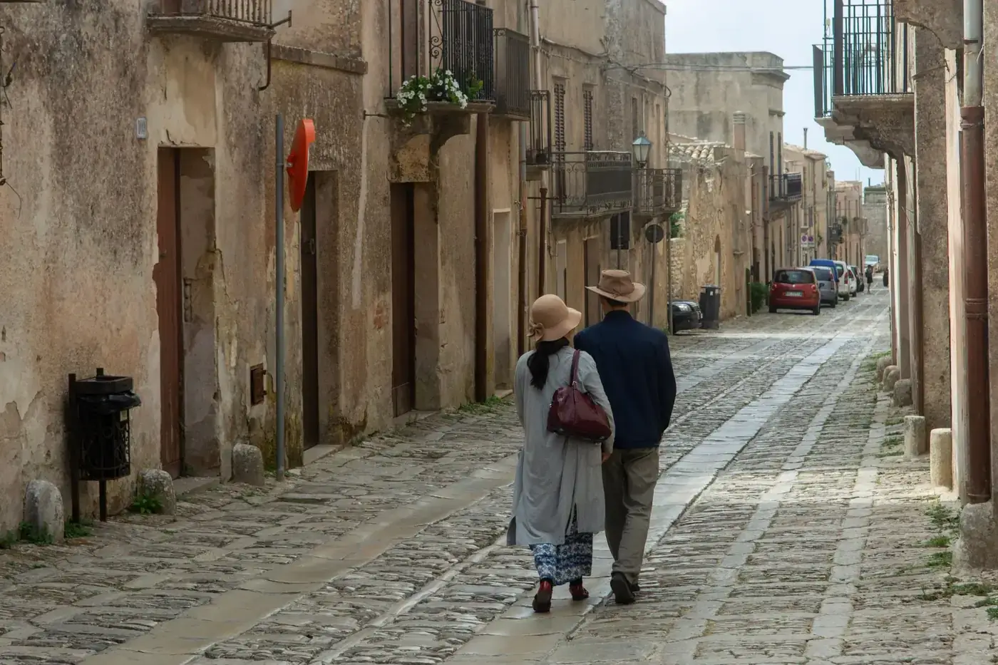 Couple walking on a cobblestone street in Erice, Sicily, showcasing charming historical architecture.