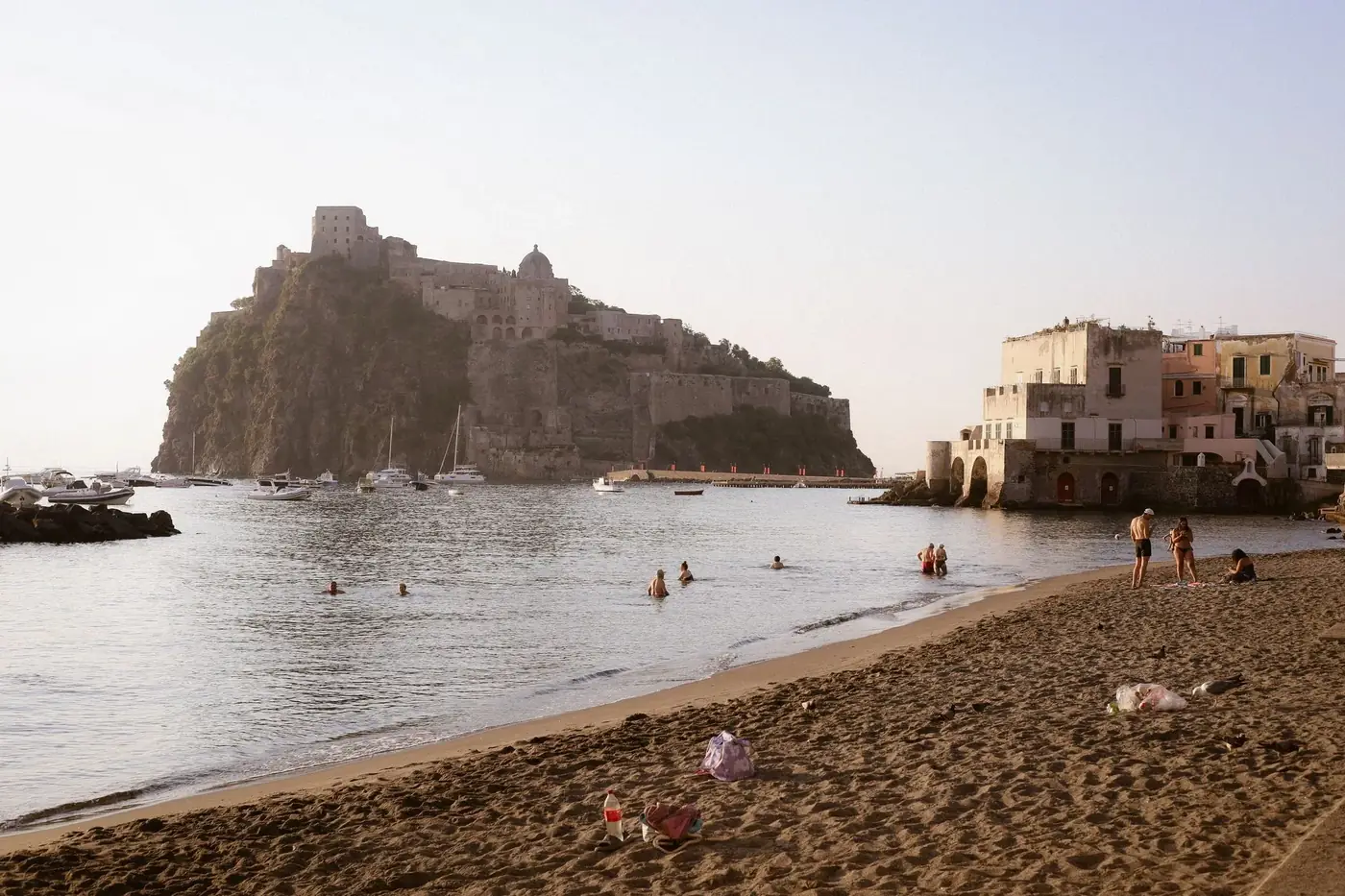 Scenic view of Aragonese Castle from Ischia beach with people enjoying the seaside.