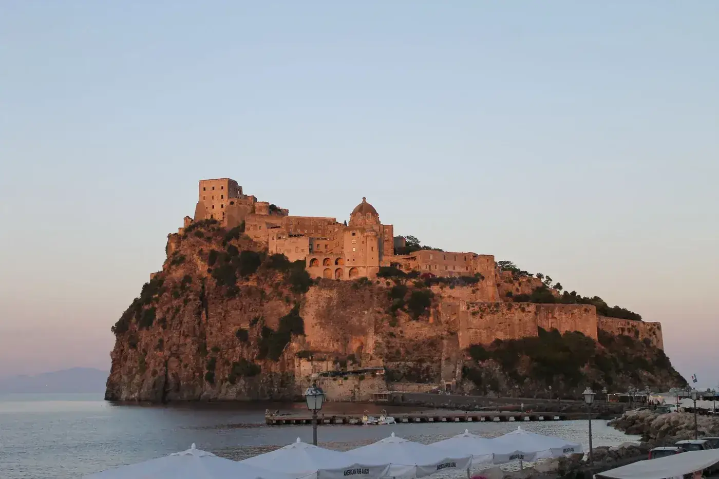 Capture the breathtaking Aragonese Castle at sunset in Ischia, Italy, highlighting its historical charm and stunning setting.