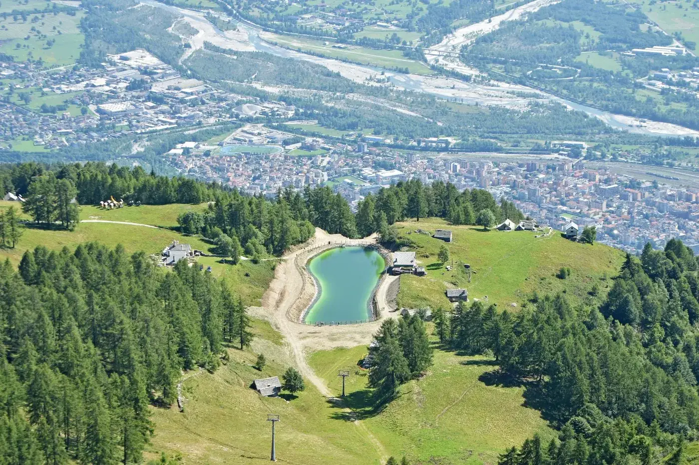 Stunning aerial view of an alpine landscape with lush greenery and a tranquil lake.