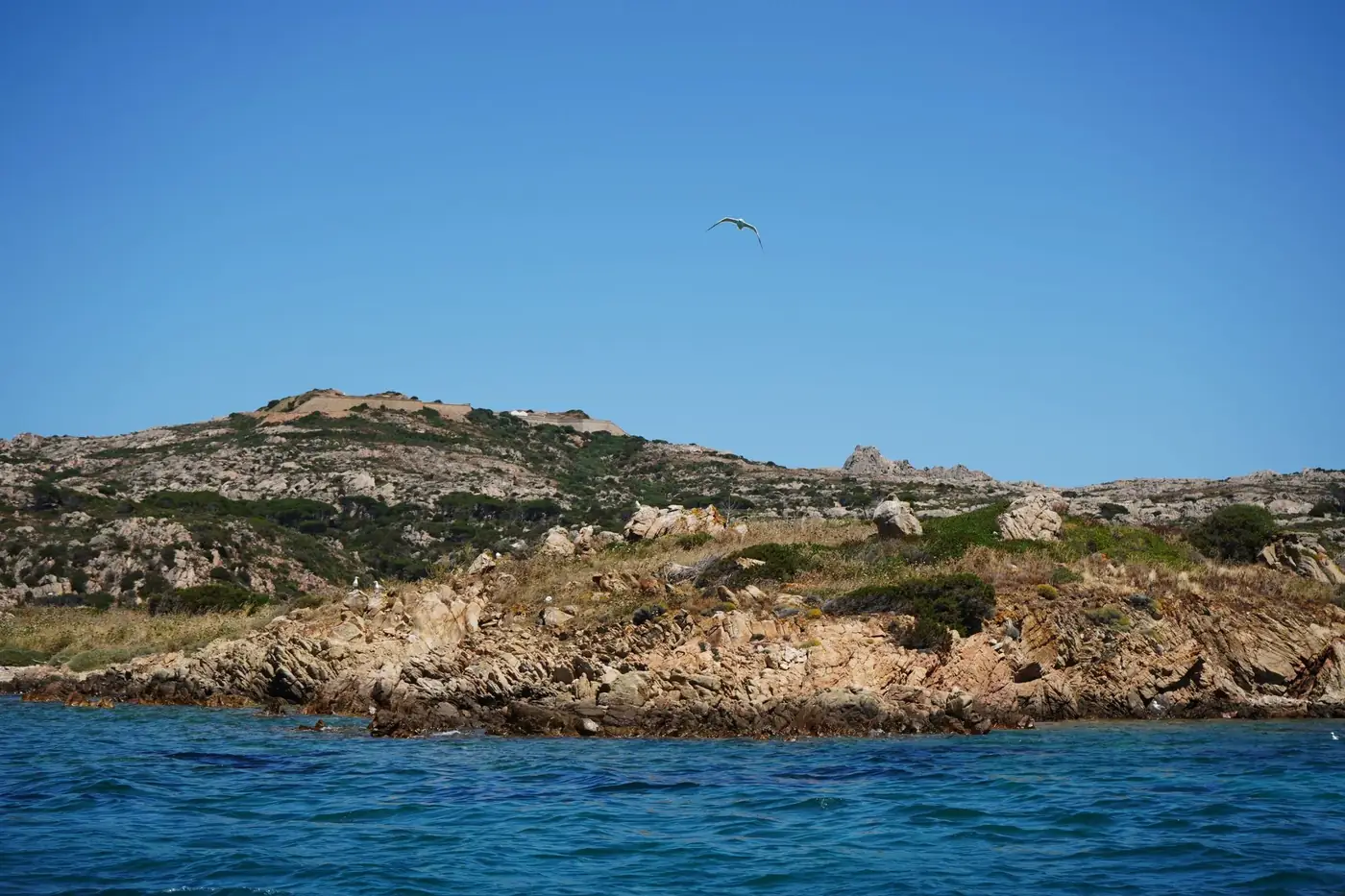 Breathtaking rocky coastline of Sardinia, Italy with clear skies and tranquil ocean waters.