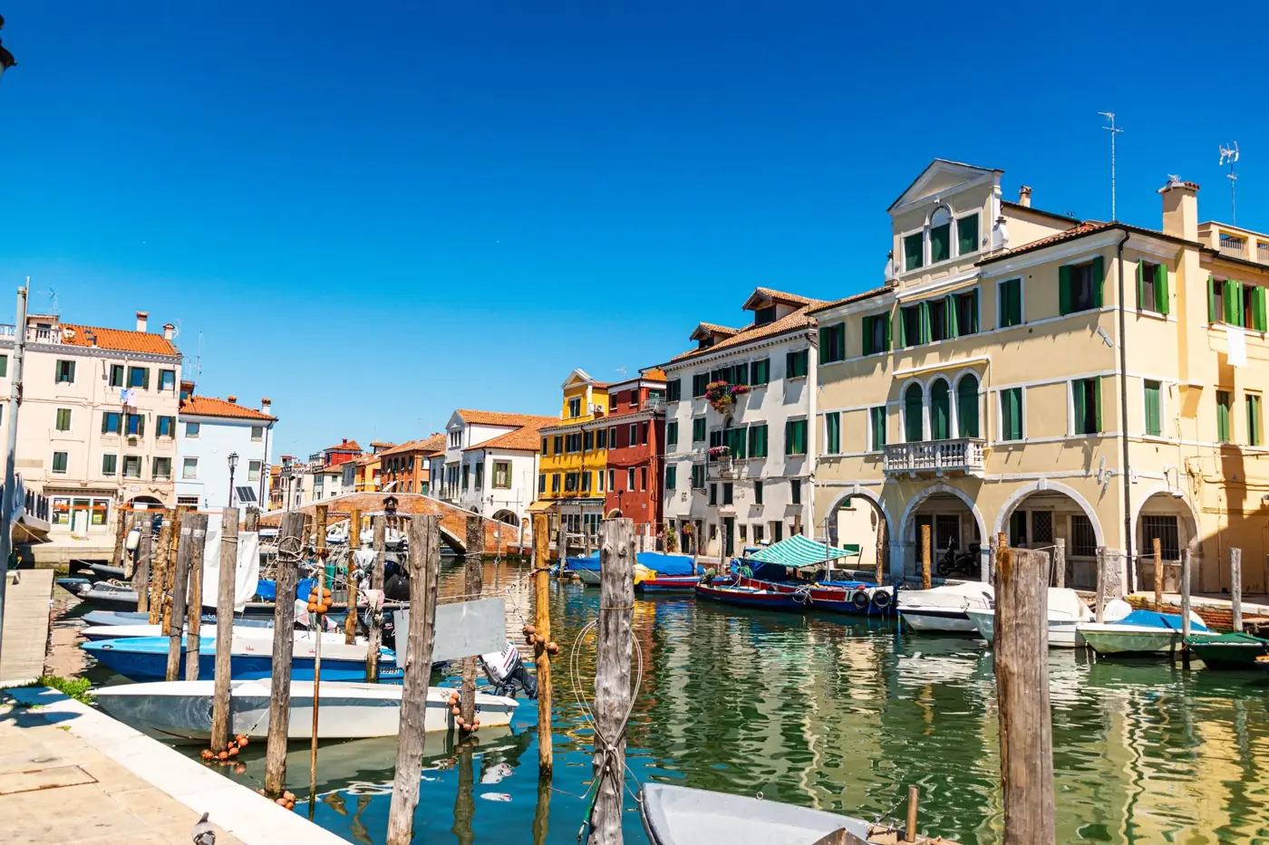 Sunny day at the vibrant canals of Chioggia, Italy with colorful buildings and boats.