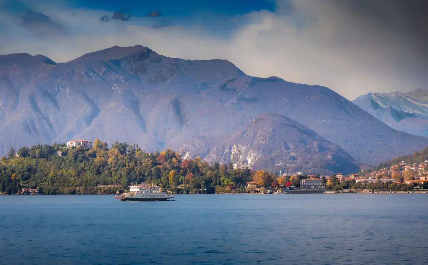 Ferry crossing Lake Maggiore with mountainous backdrop in fall, Italy.