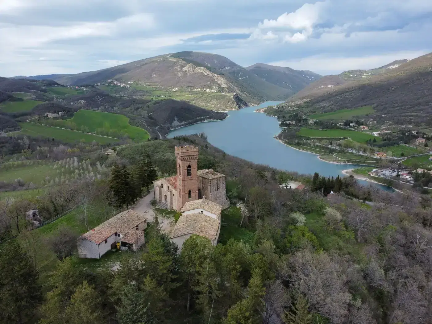Scenic aerial view of a historic castle on a hill overlooking a beautiful lake and lush valley.