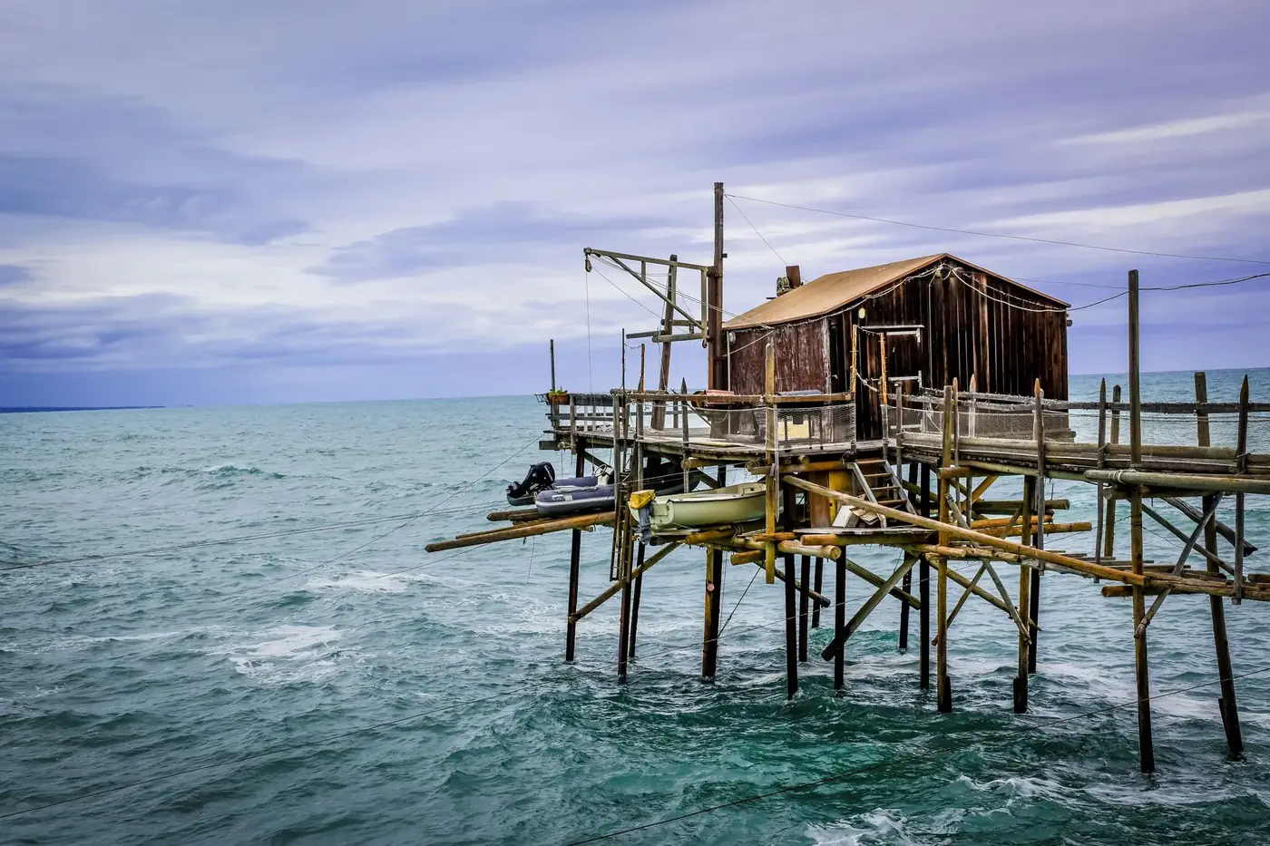 A traditional fishing hut on a wooden pier over the ocean, reflecting a serene seascape.