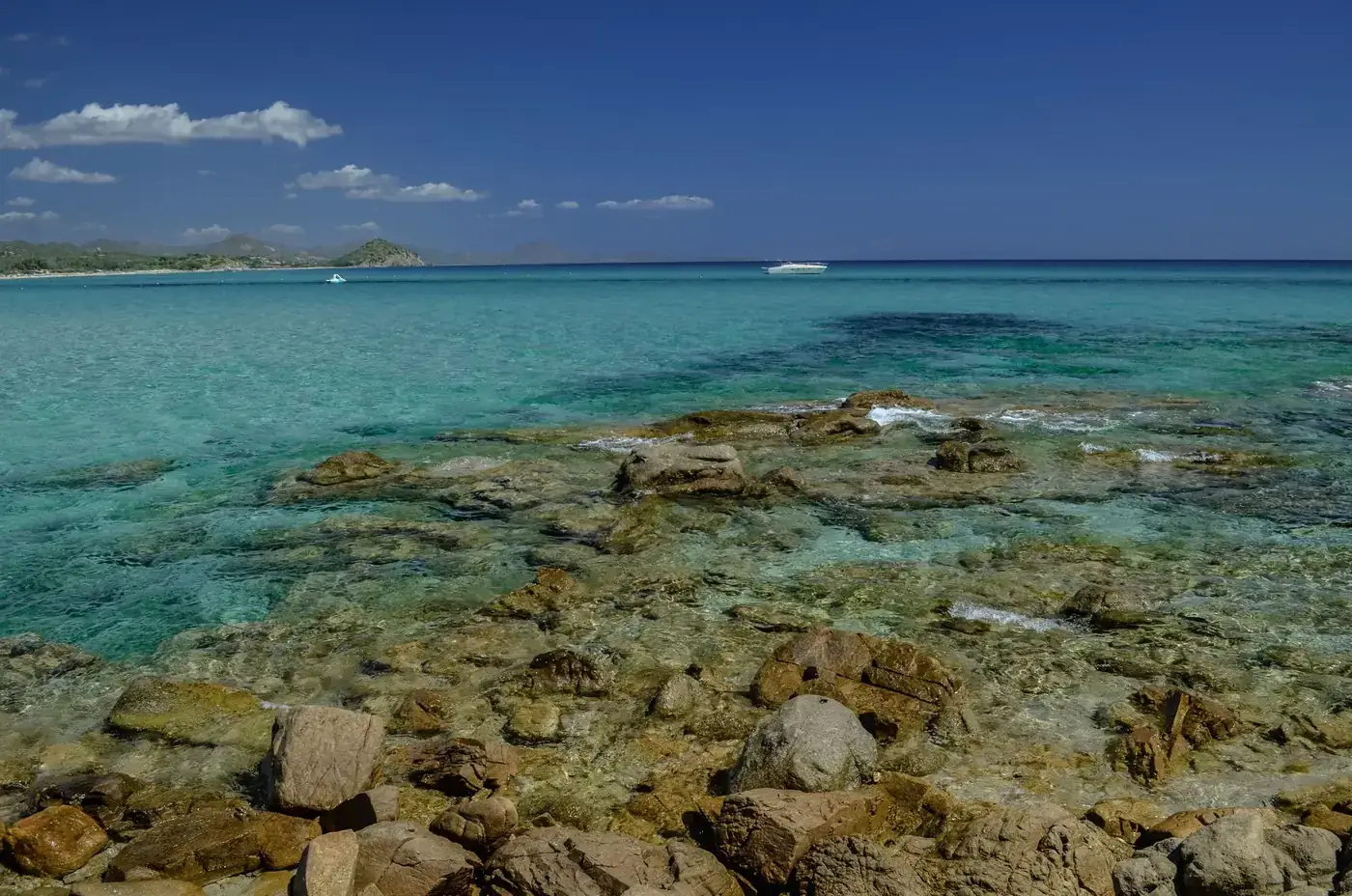 Stunning clear turquoise waters and rocky shores of a Sardinian beach under a bright blue sky.