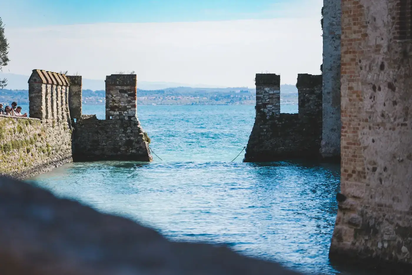 Ancient stone castle wall with towers overlooking a serene lake in Riva del Garda, Italy.