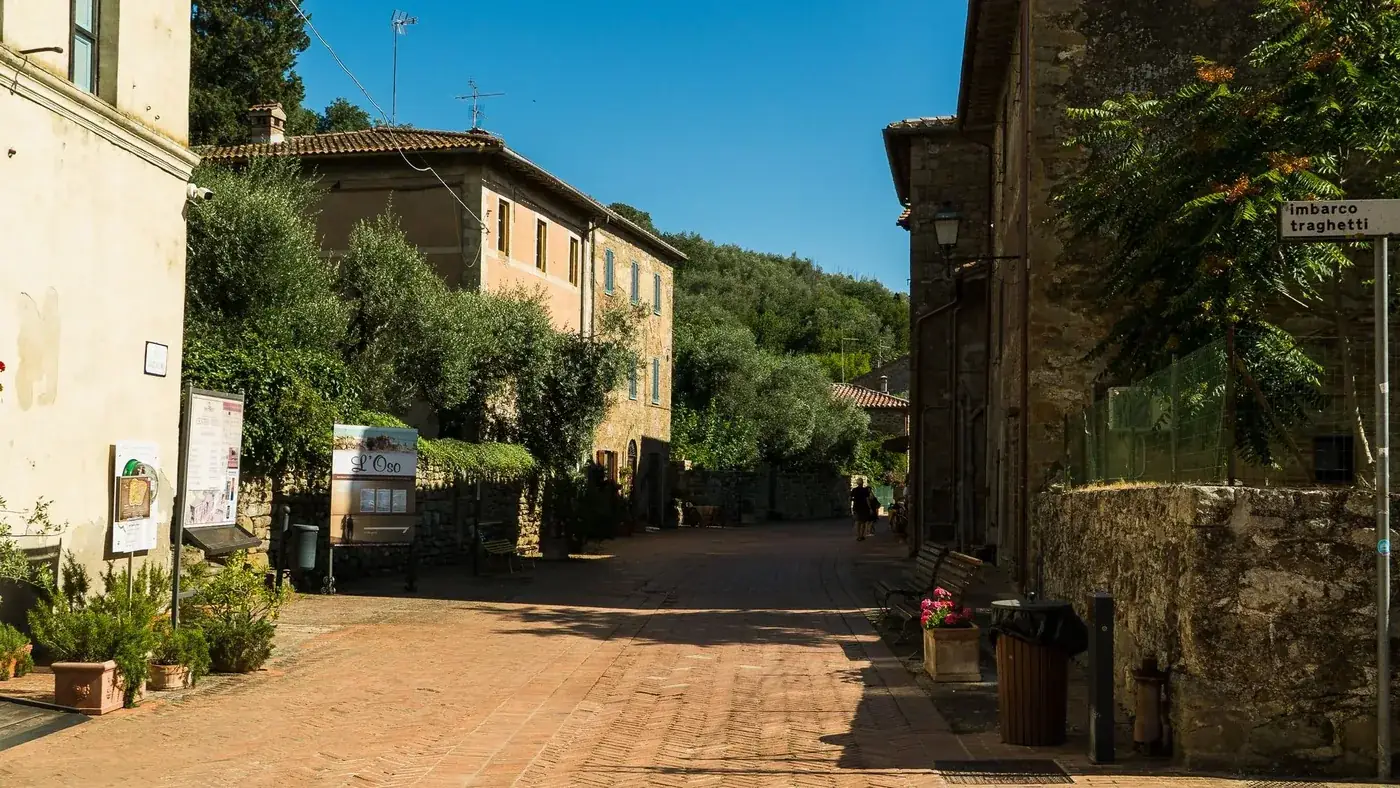 Scenic small town street in Umbria, Italy with rustic architecture and lush greenery under a bright blue sky.