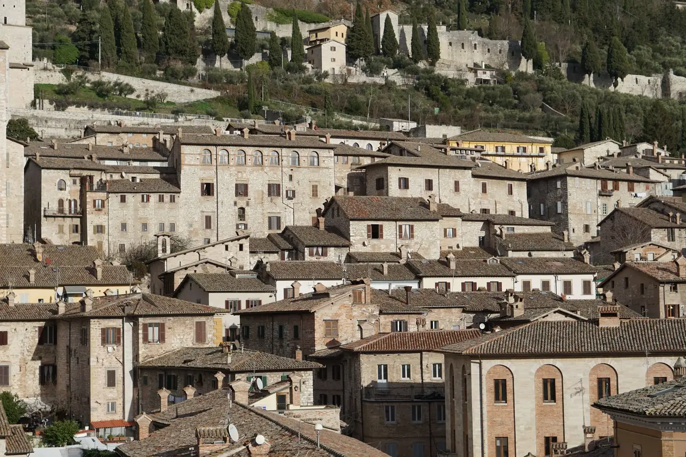A picturesque scene of ancient architecture and rooftops in Gubbio, Italy, set against a hilly backdrop.