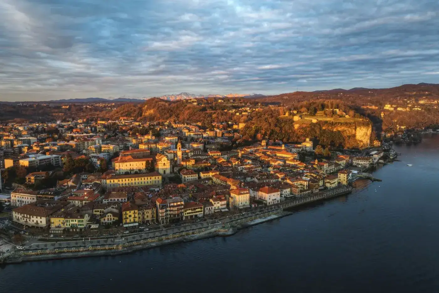 Stunning aerial view of Angera with sunset hues over Lake Maggiore, highlighting historic architecture and lush landscapes.