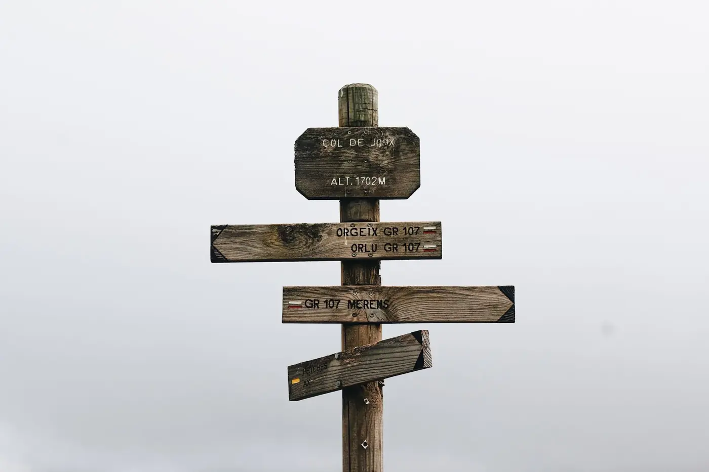 Vintage wooden signpost in foggy mountain landscape, indicating hiking trails and altitudes.