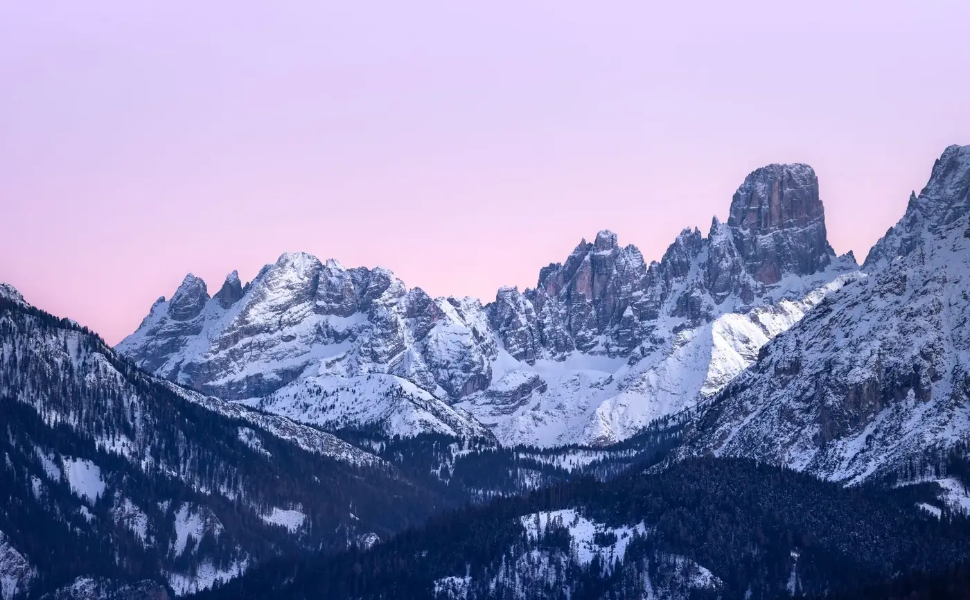 Breathtaking view of the snow-capped Dolomites at sunset with a vibrant pink sky.